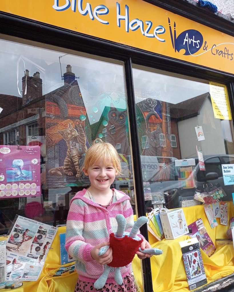 Lucy, the competition winner, standing with her toy in front of Blue Haze Arts and Crafts shop