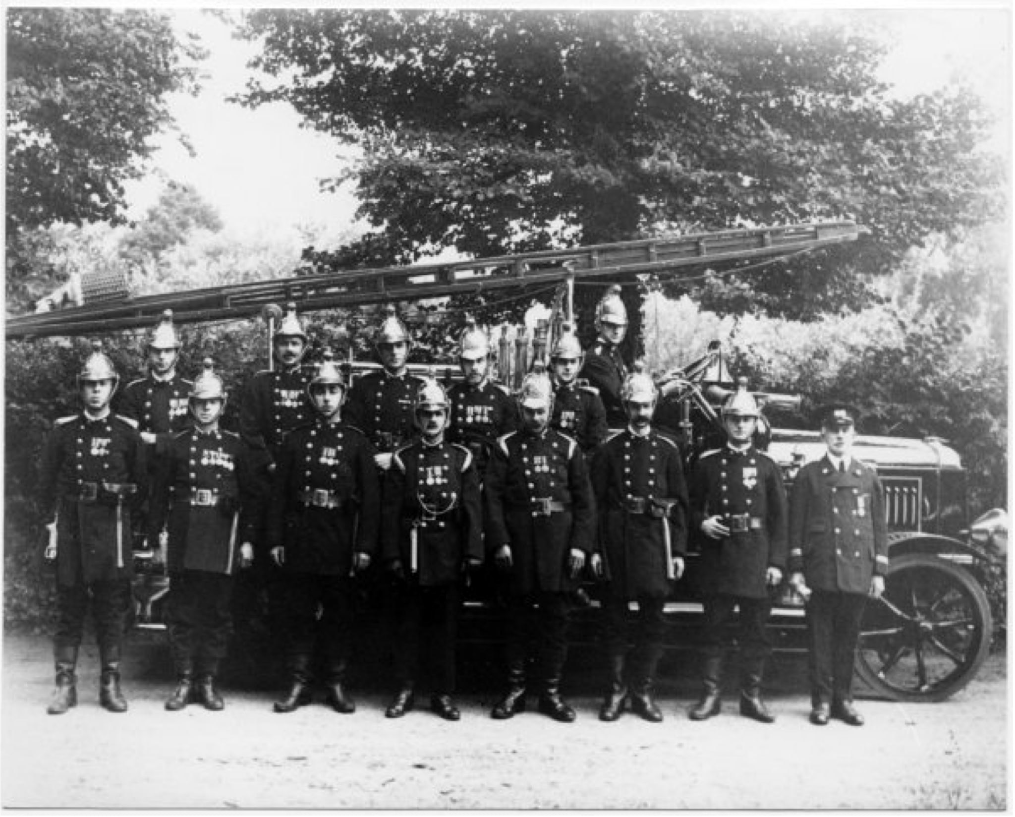 A black and white photo of fire men standing in front of the first motorised fire engine
