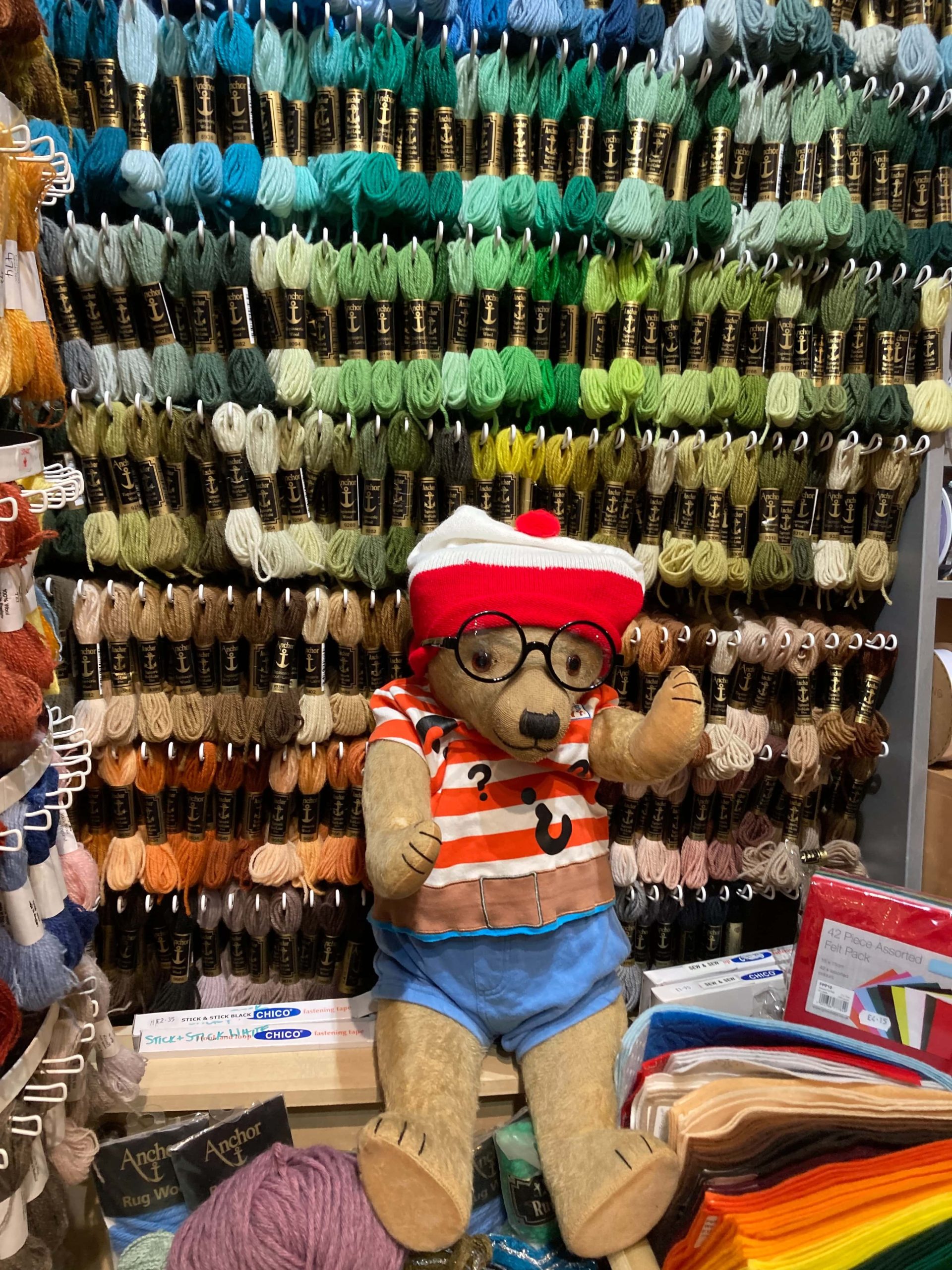 Winifred with a striped hat and shirt sitting in front of racks of wool and next to felt