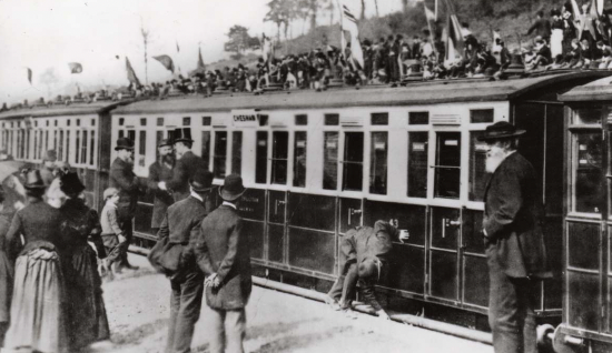 Black and white image of people on a platform celebrating with 3 train carriages in view