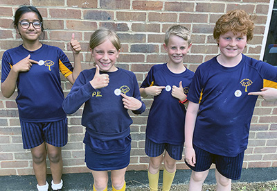 4 schools children pointing to stickers on their tops and holding their thumbs up