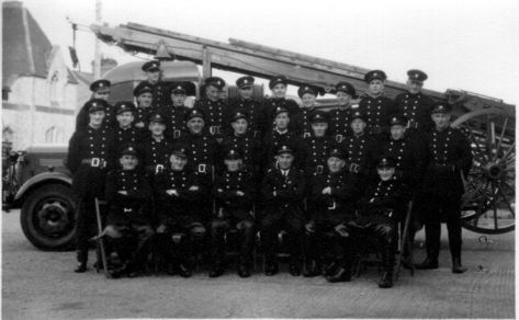 Black and white photo of firemen standing alongside the fire engine
