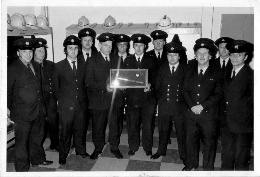 A black and white photo of firemen holding an axe enclosed in a glass box
