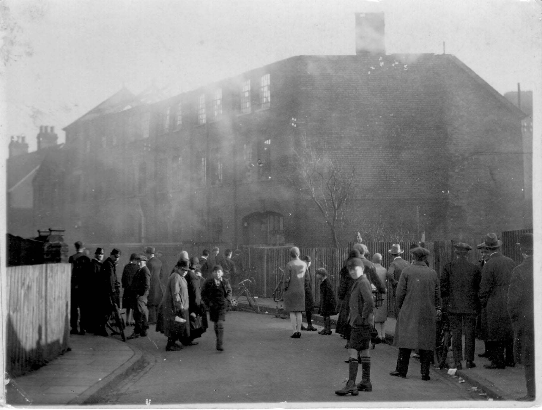 Black and white photo of a building on fire with onlookers