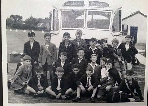 Schoolboys seated on the ground in front of a bus