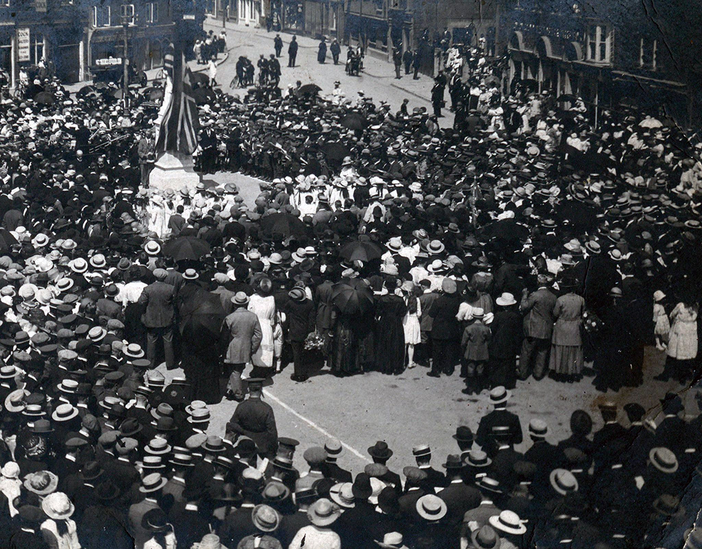 Unveiling of the war memorial. The memorial is covered in the Union Flag with many people surrounding it