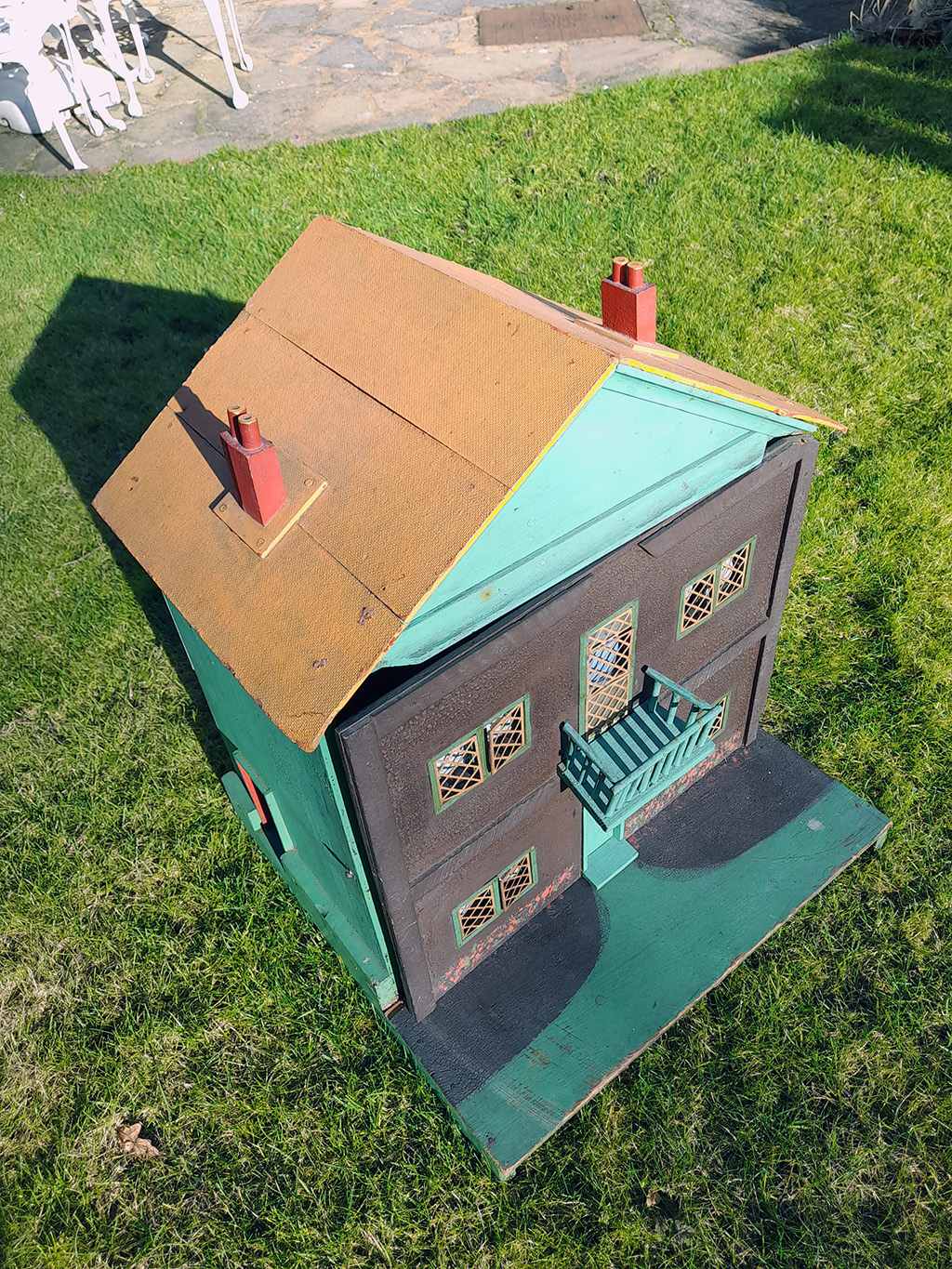 Doll's house painted green with a dark charcoal coloured front and brown roof which has 2 chimneys