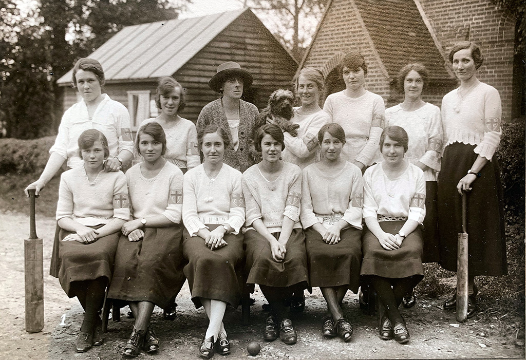 A photo of St George's Ladies Cricket Team - 6 women seated with 7 women stood behind them; 2 with cricket bats and a 3rd holding a dog