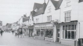 Black and white photo of the High Street shop fronts with people walking around the pedestrian area 