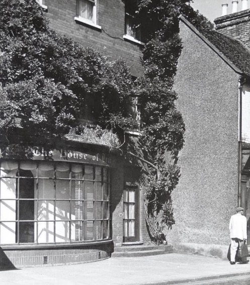 Black and white photo of a shop with a bay window and its exterior covered by wisteria