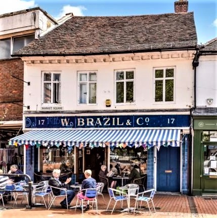 Photo of W Brazil & Co. It has a blue and white striped awning with tables and chairs below it where customers are seated