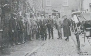 Men gather for a photo outside a building and next to a horse's cart