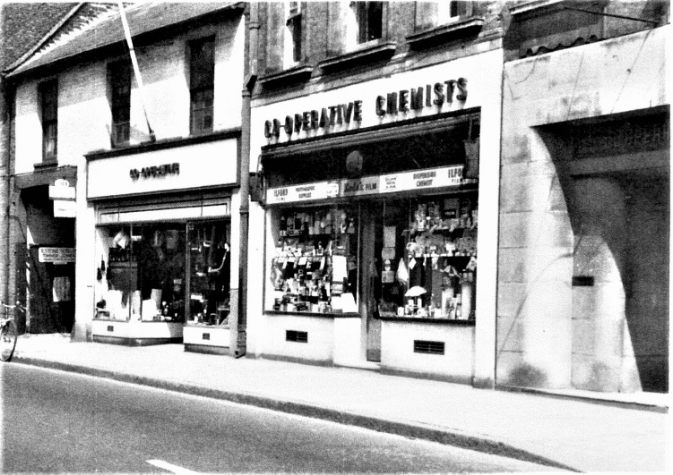 Black and white photo of some shop fronts, one of which is Co-operative Chemists