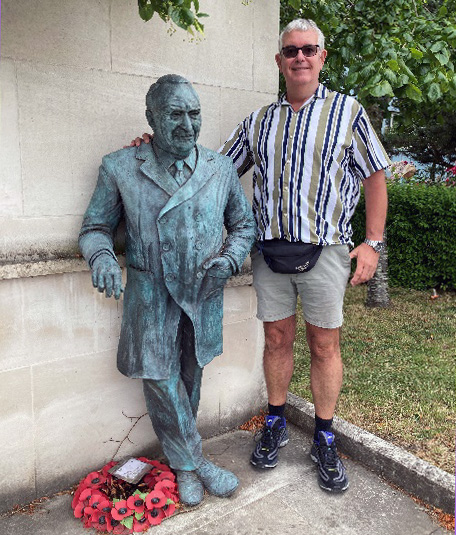 Volunteer has his photo taken next to the statue of Sir Professor Ludwig Gutterman. There is a wreath of poppies at the statue's feet.