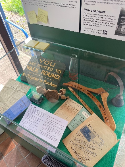 Display of some shop items from Chesham Museum's collection, including paper bag and wooden coat hanger.