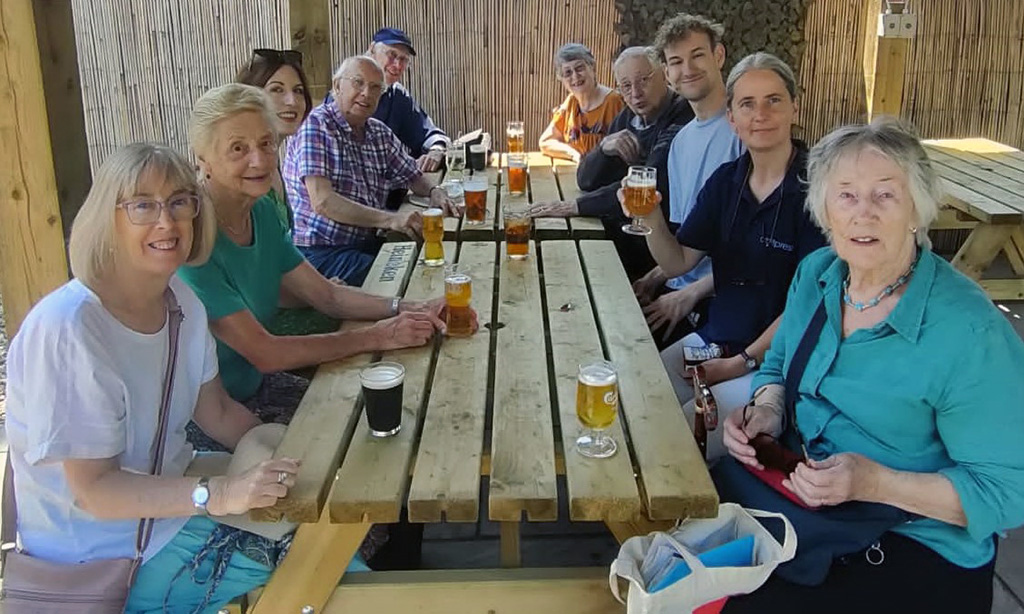 Chesham Museum volunteers gather around some wooden picnic tables enjoying a drink