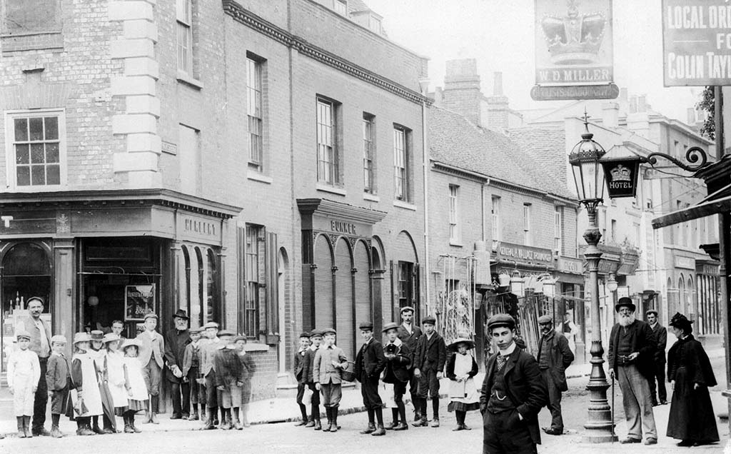 Black and white photo of people walking around Chesham with a pub and several shops in the background