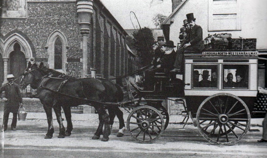Horse Bus  with driver and others seated on top. There are 2 horses pulling it and a sign on the coach says London North-Western Railway