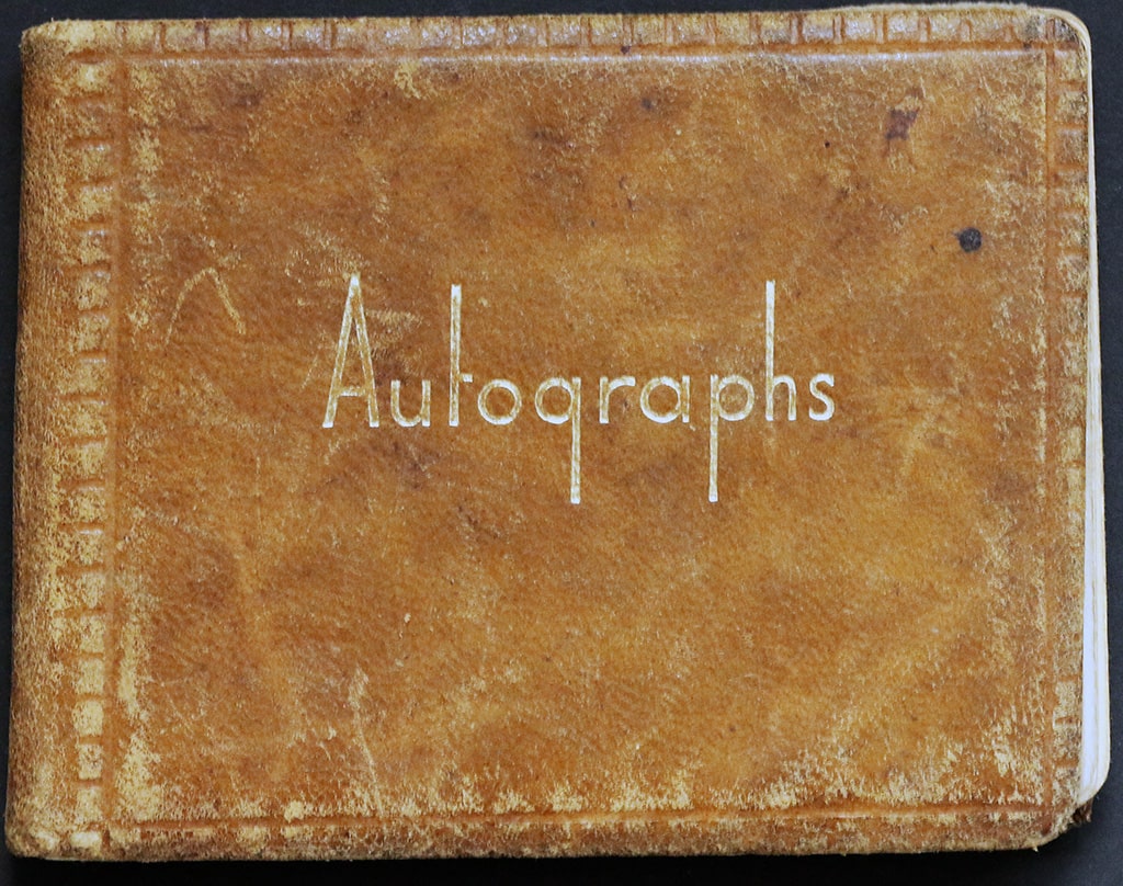 An autograph book with a worn, brown material cover