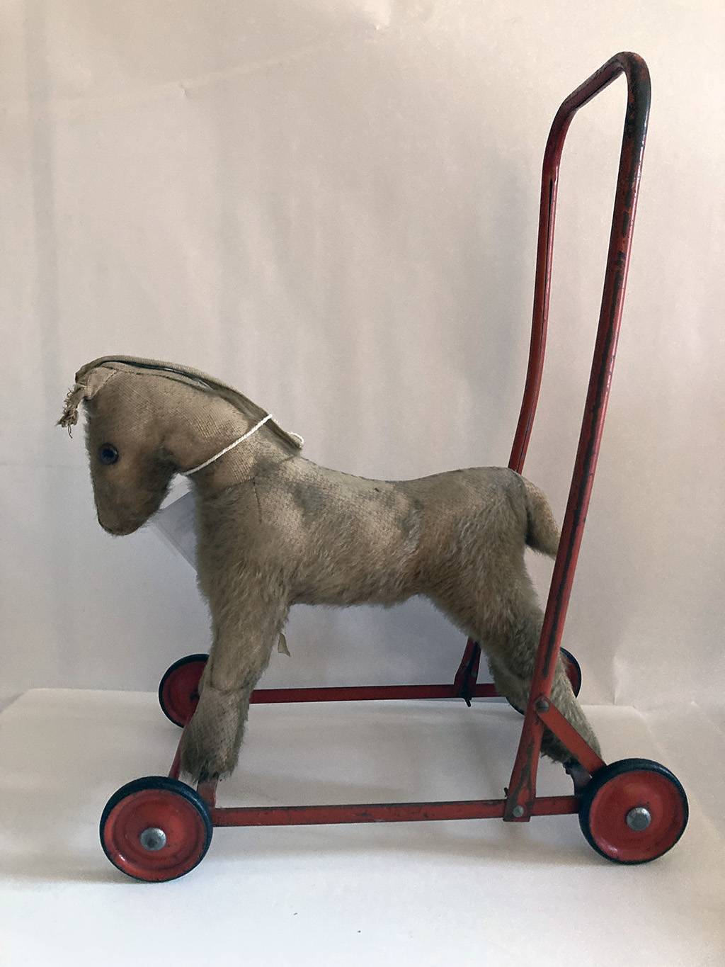 A pull along toy horse with 4 wheels and a large  red metal handle