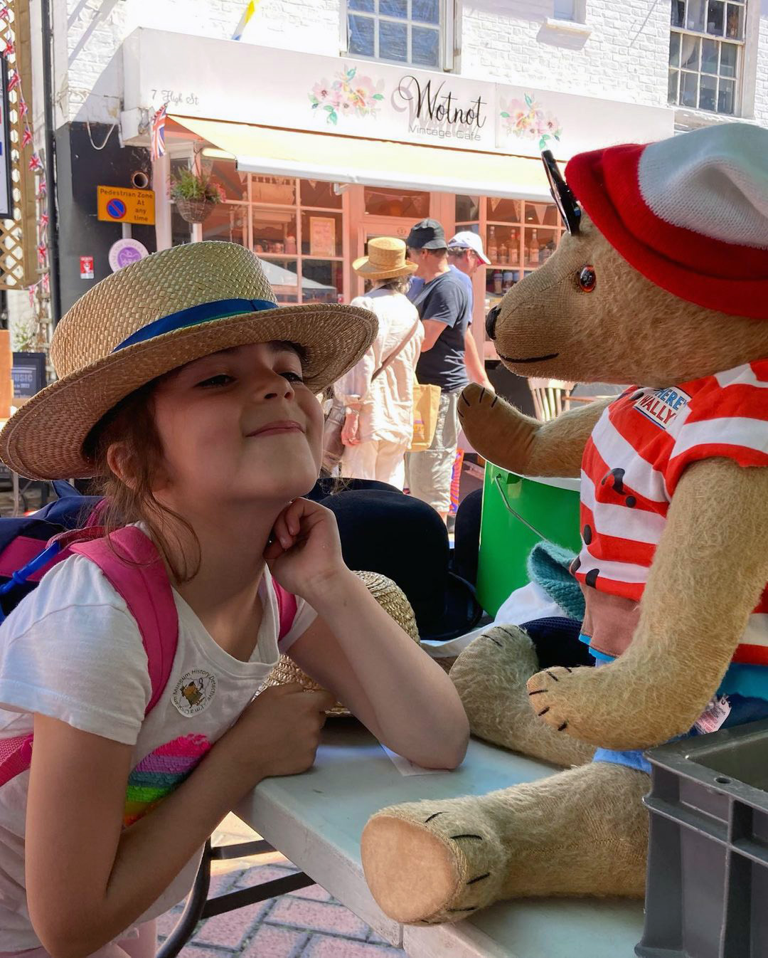 A young girl with a straw hat looks up at Winifred the bear mascot